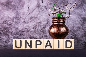 Word UNPAID made with wood building blocks on a gray background