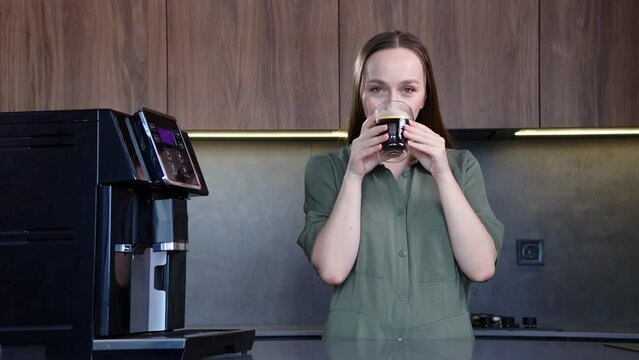 Happy woman enjoying fresh aromatic coffee near modern machine in kitchen.