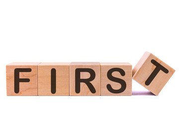 Word FIRST is made of wooden building blocks lying on the table and on a light background. Concept.