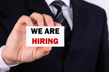 American businessman holds a card with the text We Are Hiring. Business concept