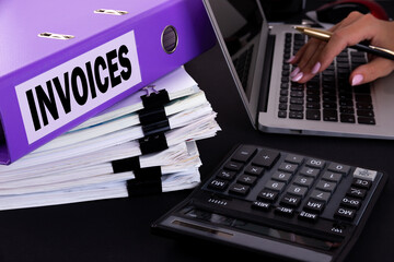 Text, word Invoices is written on a folder lying on documents on an office desk with a laptop and a...