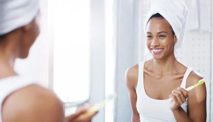  Woman, mirror and brushing teeth in bathroom with smile or towel after shower for hygiene, cleaning or oral care. Female person, reflection and home for healthy mouth or tooth dental, gums or routine © peopleimages.com