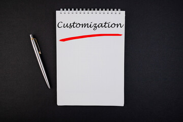 The text, the word Customization, is written in a notebook lying on a black table with a pen....
