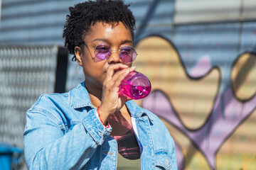 young black woman on the street drinking a bottle of soda