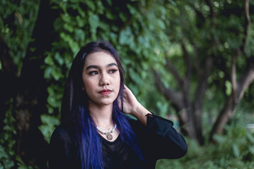 Young woman with blue hair in goth attire posing in a lush forest setting