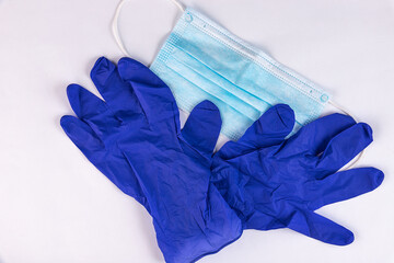 A pair of thin blue medical latex gloves and face shield on a white background. Disposable rubber...