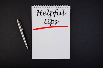 The text, the word Helpful Tips, is written in a notebook lying on a black table with a pen....