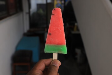Hand holding watermelon shaped summer ice lolly on blurry background