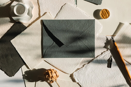 Overhead view of a blank piece of homemade deckle edge card, calligraphy pen, envelope and flowers on a table in sunlight