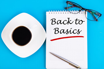 The text, the inscription, the phrase Back to Basics is written in a notebook that lies on a blue table with a cup of coffee, glasses and pen. Business concept.