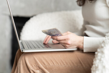 Close-up of a woman holding a handful of cash while using a computer
