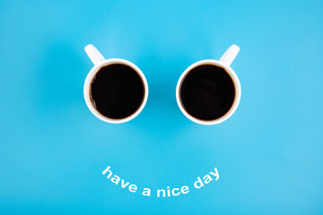 Two white coffee mugs with a smile on a blue background with the phrase Have s nice day. Happy coffee mugs.