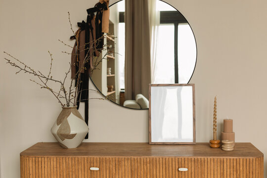 Vase, candle and blank picture frame on a sideboard with a mirror in a stylish living room