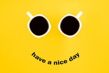 Two white coffee mugs with a smile on a yellow background with the phrase Have a nice day. Happy...