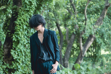 Stylish young Asian man in goth-inspired outfit standing in a lush forest