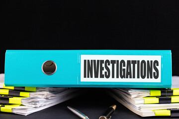 INVESTIGATIONS text is written on a folder lying on a stack of papers on an office desk. Business concept.