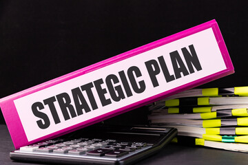 STRATEGIC PLAN text is written on a folder lying on a stack of papers on an office desk. Business...