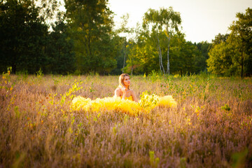 Captured at golden hour, this image features a young woman seated in a field, enveloped by the warm...