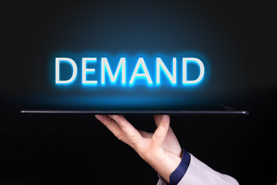 Man hand holds a tablet over which a neon text is written, the word DEMAND. Business concept. - Powered by Adobe