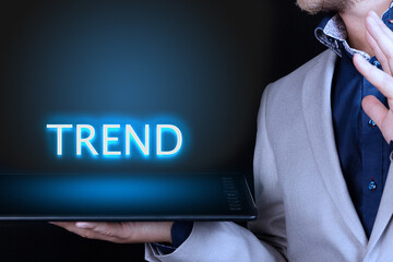 Businessman, man holds in his hand a tablet with a neon word, TREND text. Business concept.