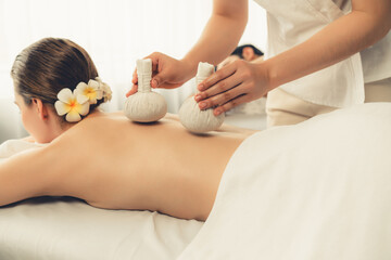 Obraz na płótnie Canvas Hot herbal ball spa massage body treatment, masseur gently compresses herb bag on couple customer body. Tranquil and serenity of aromatherapy recreation in day lighting ambient at spa salon. Quiescent