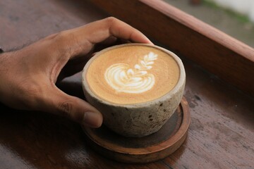 hand hold a cup of cappuccino on a brown wooden table. Great for backgrounds. text or Copy space