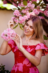 Obraz premium portrait of a blonde woman next to a blooming Japanese cherry tree on a spring day.