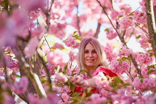 portrait of a blonde woman next to a blooming Japanese cherry tree on a spring day.