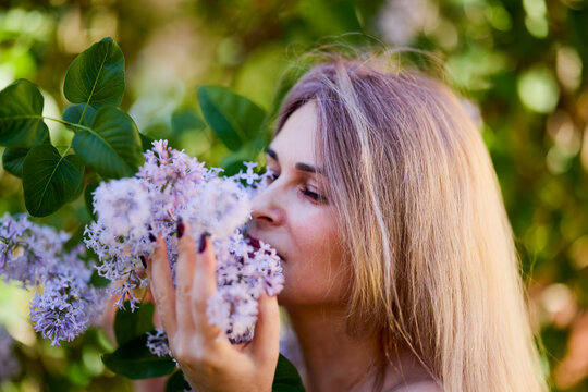 Beautiful Woman Enjoying the Smell of Lilac. Cute Model and Flowers. Aromatherapy and Spring.