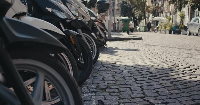 Scooter motorcycles parked Naples Italy granite paved street close up