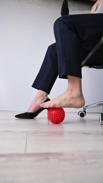 Business woman massages her feet on a massage ball with spikes. Vertical video. 