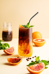 Americano coffee with orange juice (bumble) in a tall glass with ice and mint on a yellow background