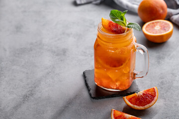 Freshly squeezed blood orange juice with ice, mint and a slice of fruit in a jar on a blue...