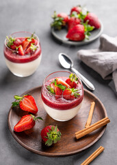 Strawberry and cream panna cotta in glasses with fresh berries on a wooden plate on a gray background.