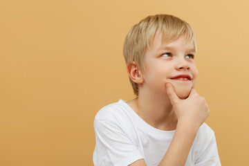 Blonde boy . Let me think . Thoughtful clever schooler in white shirt with puzzled serious expression , child thinking doubting , making choice. indoor studio shot isolated on beige background