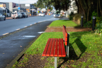 Empty red bench by the roadside. Cars on the road. Auckland.
