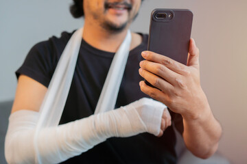 Happy middle aged man wearing a black shirt with hand injury uses smartphone.