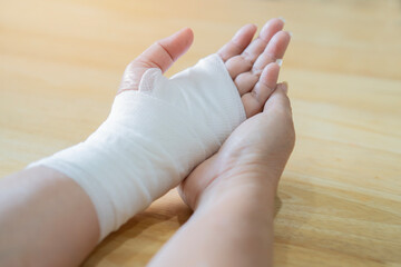 Old woman with gauze bandage wrapped around her injured hand over wooden table. First aid