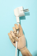 Electric cable in mannequin's hand on blue background