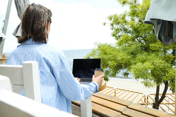 A young girl works on a laptop with a view of the sea