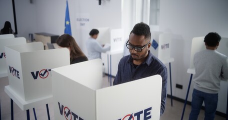 Fototapety  High angle of multiethnic European people voting at polling station during EU elections. Diverse voters fill out ballots in voting booths. Election Day in the European Union. Civic duty and democracy.