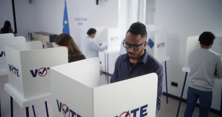 Rucksack High angle of multiethnic European people voting at polling station during EU elections. Diverse voters fill out ballots in voting booths. Election Day in the European Union. Civic duty and democracy. © Framestock