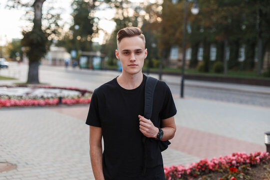 Cool fashion handsome man with a hairstyle in a black mock-up T-shirt with a backpack walks on the street