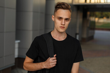 Cool handsome fashion man with a hairstyle in a fashionable black mock-up T-shirt with a backpack...