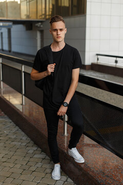 Stylish handsome fashion man model in a fashionable black T-shirt with a backpack walks on the street