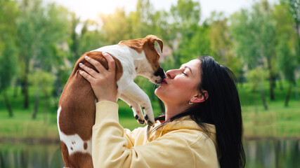 Woman and a dog close-up portraits. Woman holds a dog in her arms, hugs. Dog licks and kisses the owner. Jack russell terrier dog. Beautiful colorful summer natural landscape