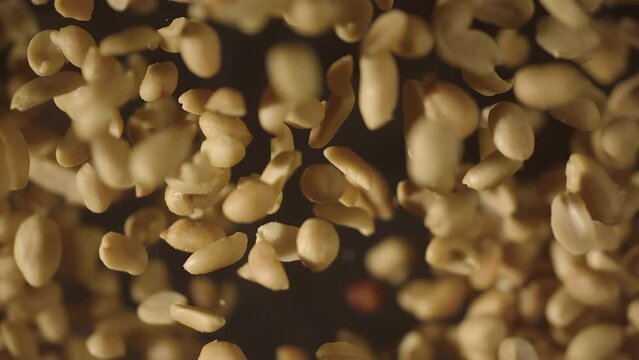 Top view of crispy roasted salted peanuts falling in super slow motion close up. Hot delicious fried peanuts snacks with smoke flying. High speed 1000 fps vertical video