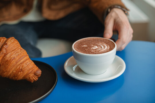 Close-up of a man sitting in a cafe eating a croissant and drinking a cup of coffee
