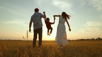 Mom dad kid hold hands at sunset. Joyful merry happy family together kid child boy playing jumping...