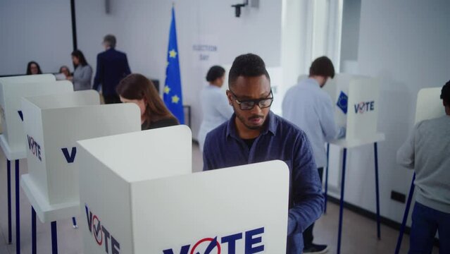 High angle of multiethnic European people voting at polling station during EU elections. Diverse voters fill out ballots in voting booths. Election Day in the European Union. Civic duty and democracy.